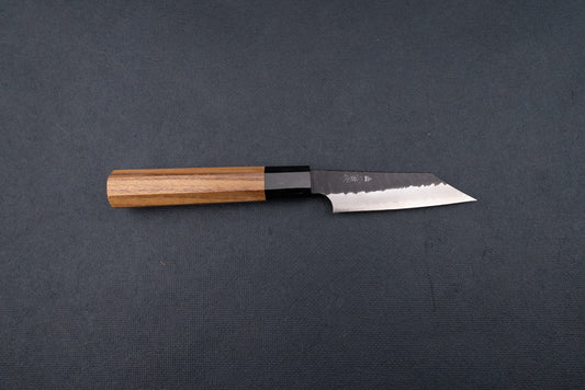 Nigara SG2 Kurouchi Tsuchime Kiritsuke Petty 95mm, a Japanese-style kitchen knife featuring a hammered single-bevel blade and octagonal wooden handle, displayed on a dark cloth backdrop.