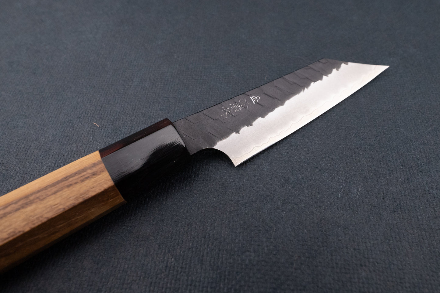 Nigara SG2 Kurouchi Tsuchime Kiritsuke Petty 95mm knife with a hammered finish and octagonal wooden handle, perfect for precise cutting tasks, displayed on a dark mat.
