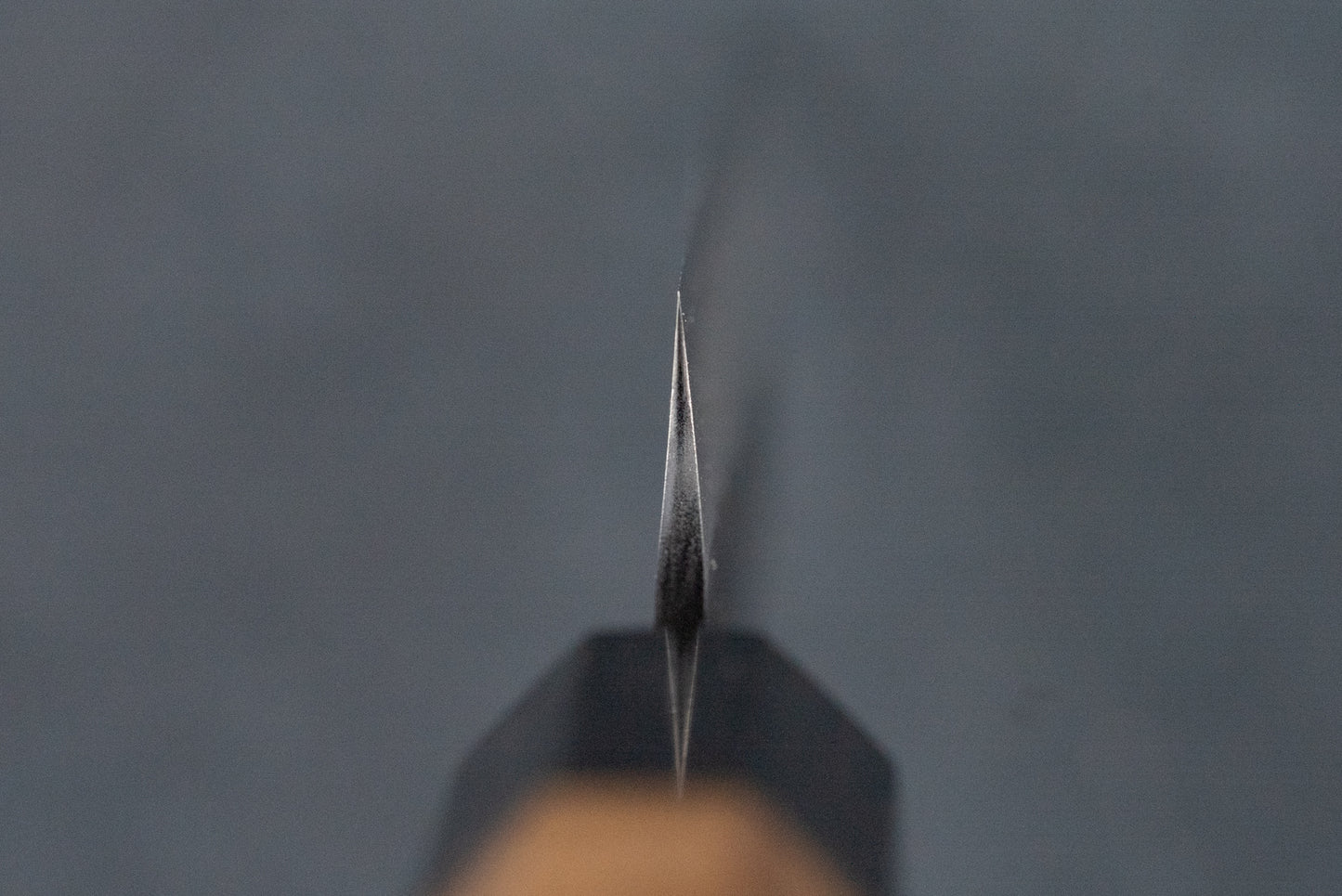 Close-up of the sharpened edge of the Nigara SG2 Kurouchi Tsuchime Kiritsuke Petty 95mm knife, highlighting its precision craftsmanship, ideal for delicate tasks on a cutting board. Handle blurred in the background.