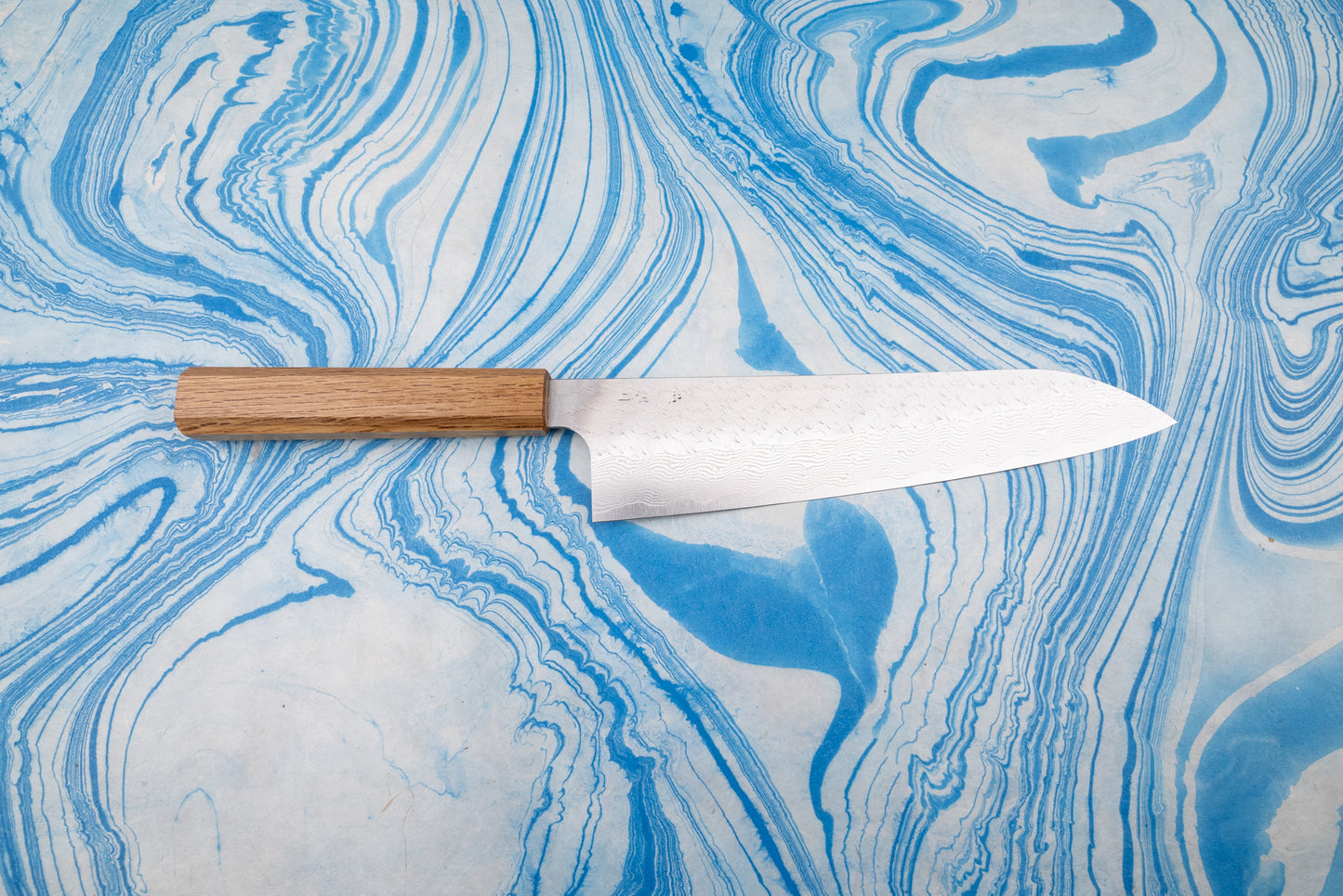 Nigara SPG STRIX Tsuchime Damascus Gyuto 240mm, showcasing a beautifully crafted Japanese-style blade with a subtle Damascus pattern, laid flat with a straight wooden handle on a marbled surface.