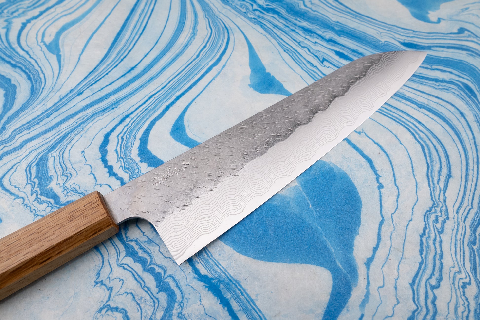 Nigara SPG STRIX Tsuchime Damascus Gyuto 240mm, featuring a patterned steel blade and wooden handle, showcased on a marbled background, epitomizing Japanese craftsmanship from Knifewear's exclusive selection.