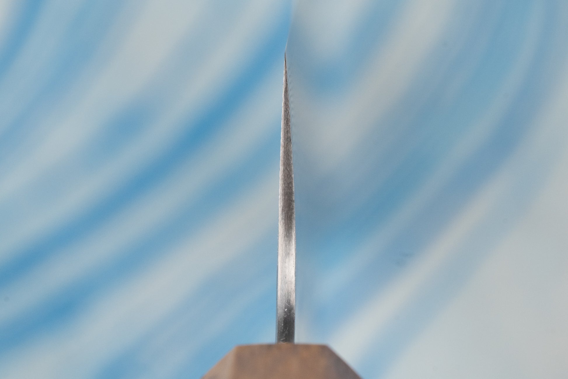 Extreme close-up of the sharpened cutting edge of a Nigara SPG STRIX Tsuchime Damascus Nakiri 180mm, showcasing its precision craftsmanship, with a hint of the wood-toned handle visible.