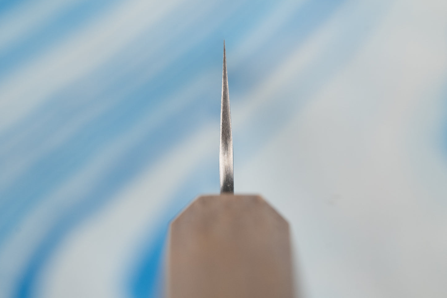 Close-up of the sharpened tip of the Nigara SPG STRIX Tsuchime Damascus Petty 120mm knife, standing upright on a sharpening stone, highlighting its precise craftsmanship for delicate kitchen tasks.