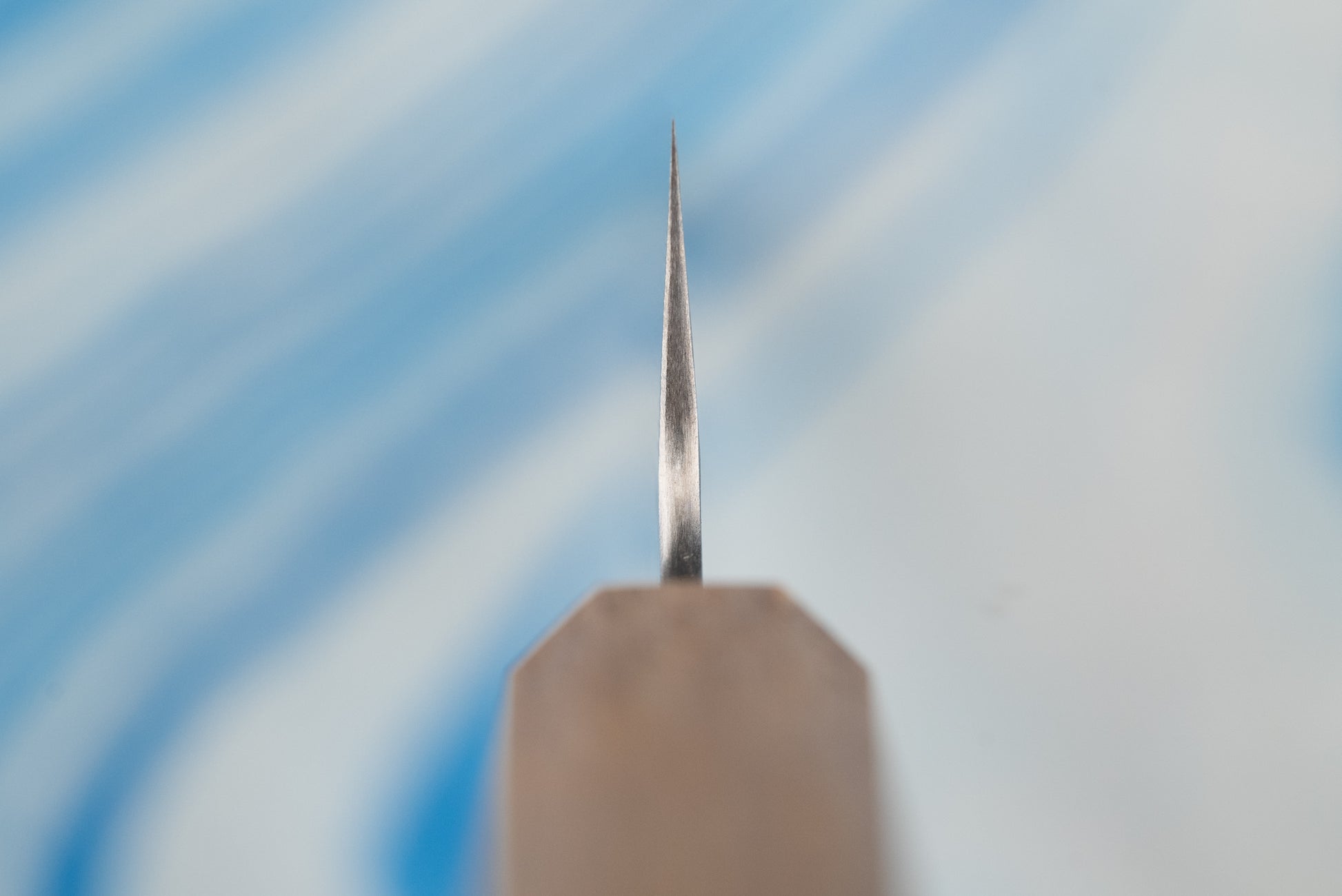 Close-up of the sharpened tip of the Nigara SPG STRIX Tsuchime Damascus Petty 120mm knife, standing upright on a sharpening stone, highlighting its precise craftsmanship for delicate kitchen tasks.
