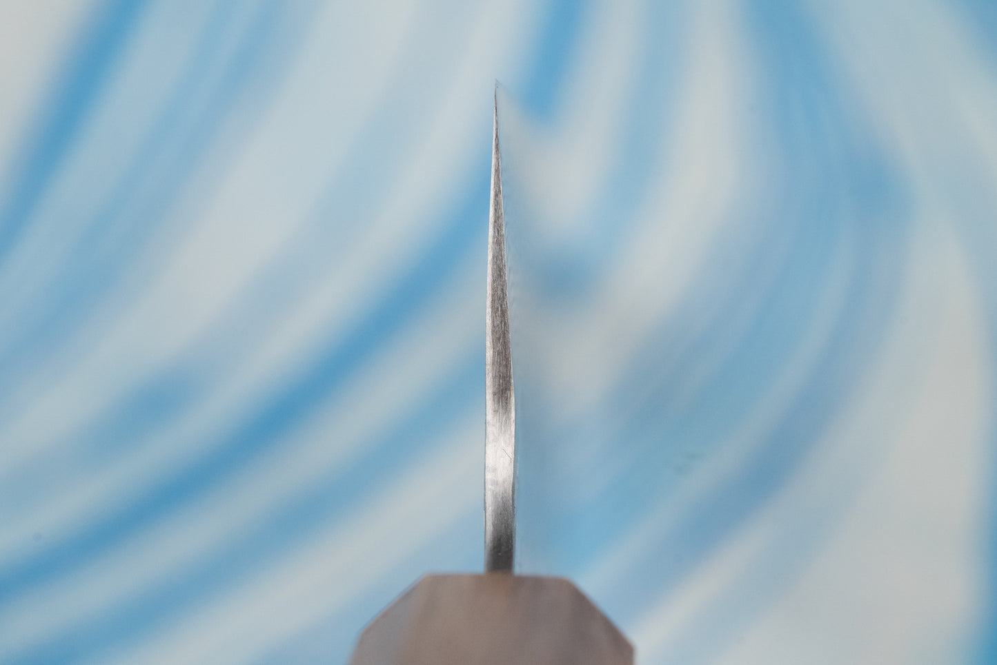 Close-up of the Nigara SPG STRIX Tsuchime Damascus Santoku 165mm knife, showcasing its razor-thin, sharpened metal edge. Part of the handle is visible, emphasizing precision and craftsmanship.