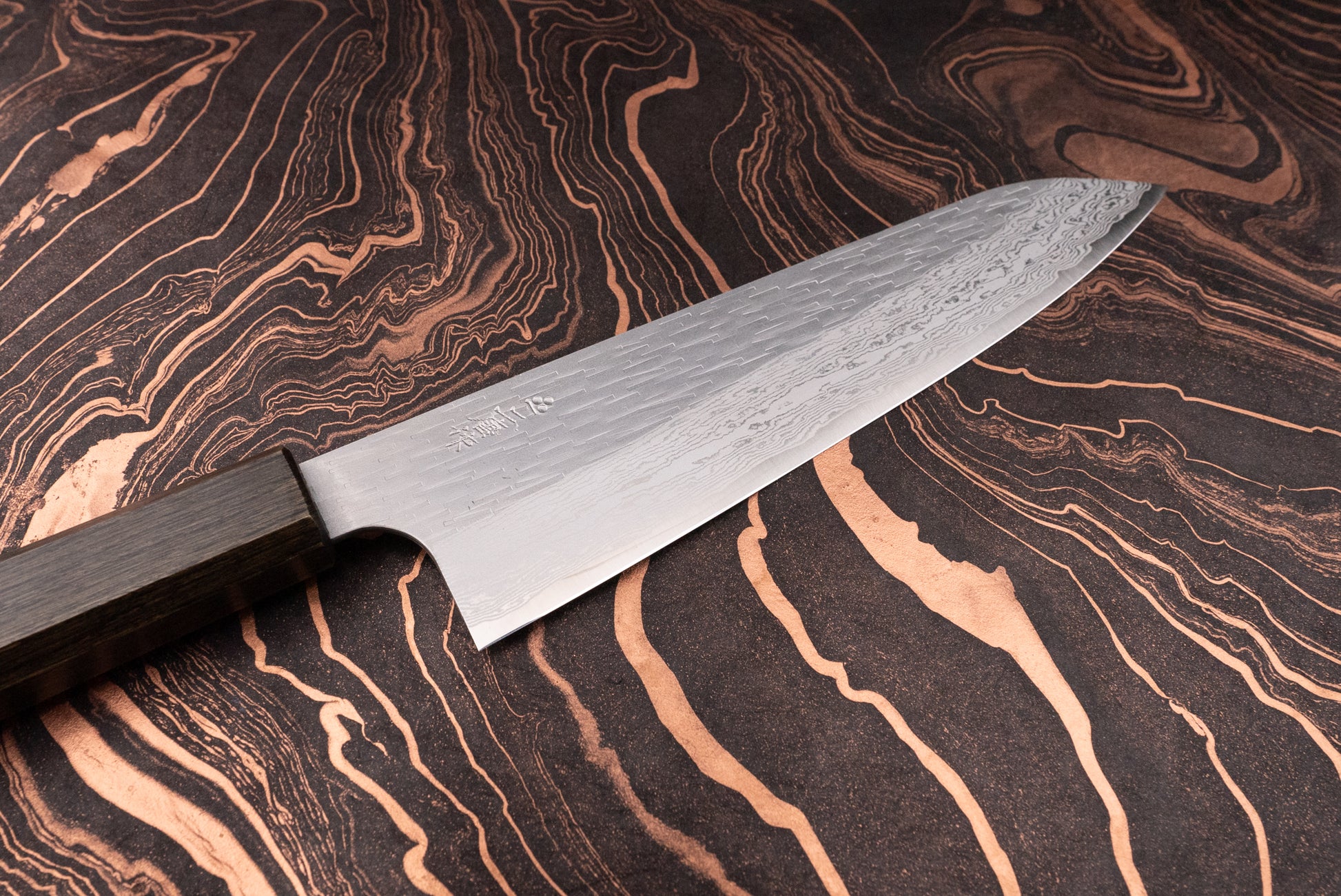 Nigara VG XEOS Tsuchime Damascus Gyuto 225mm, showcasing a Damascus-pattern blade with visible layering and a dark wooden handle, elegantly displayed on a black-and-copper marbled surface, embodying Japanese craftsmanship.