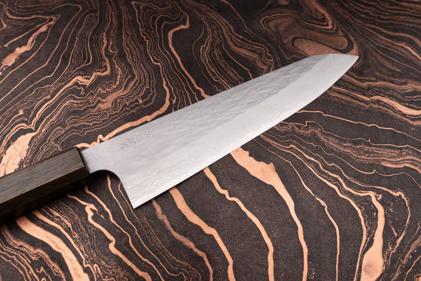 Nigara VG XEOS Tsuchime Damascus Gyuto 255mm features a Damascus-pattern steel blade and an octagonal wooden handle, elegantly displayed on a marbled board, ideal for versatile kitchen tasks.