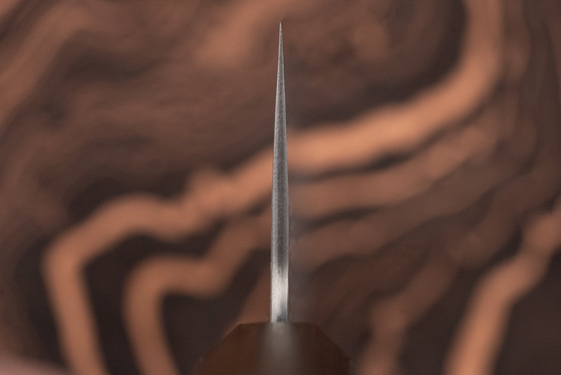 Close-up of the Nigara VG XEOS Tsuchime Damascus Nakiri 180mm blade's tip, highlighting its precise craftsmanship, with a blurred wood grain background, emphasizing exceptional Japanese steel artistry.