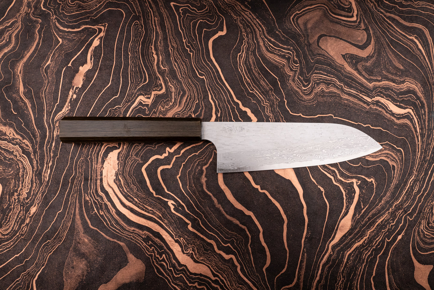 Nigara VG XEOS Tsuchime Damascus Santoku 185mm knife with a dark wooden handle, featuring a damascus-patterned steel blade, displayed on a black-and-copper marbled surface, showcasing its craftsmanship and design.