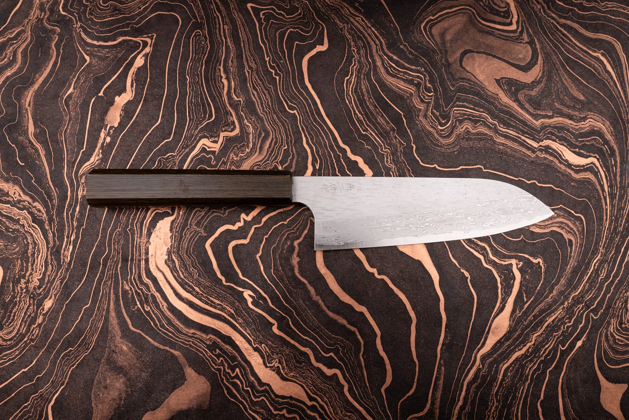 Nigara VG XEOS Tsuchime Damascus Santoku 185mm knife with a dark wooden handle, featuring a damascus-patterned steel blade, displayed on a black-and-copper marbled surface, showcasing its craftsmanship and design.