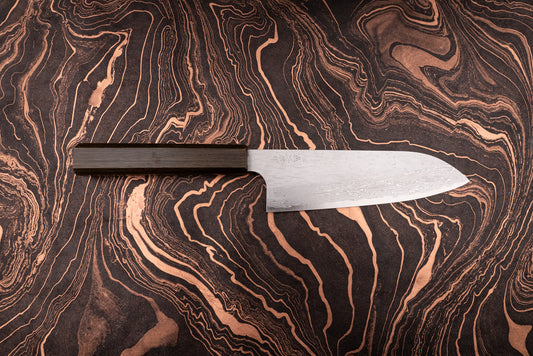 Nigara VG XEOS Tsuchime Damascus Santoku 185mm knife with a dark wooden handle, featuring a damascus-patterned steel blade, displayed on a black-and-copper marbled surface, showcasing its craftsmanship and design.