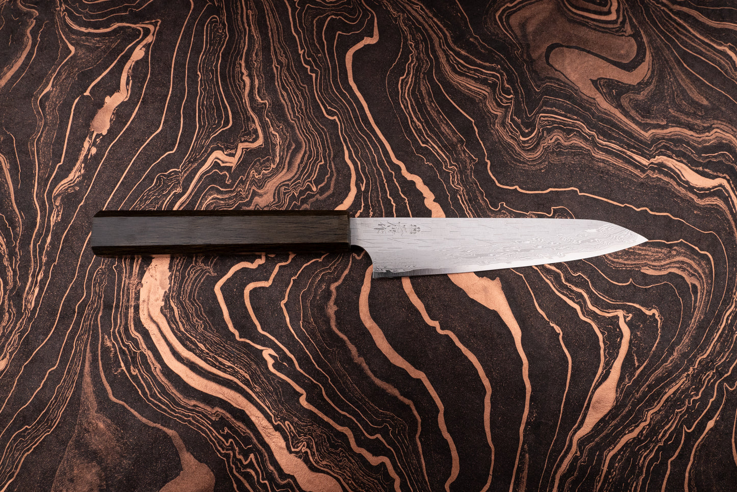 Nigara VG XEOS Tsuchime Damascus Petty 160mm knife with a slender damascus-patterned blade and dark wooden handle, positioned on a dark, marbled surface, showcasing its elegant, handcrafted design.