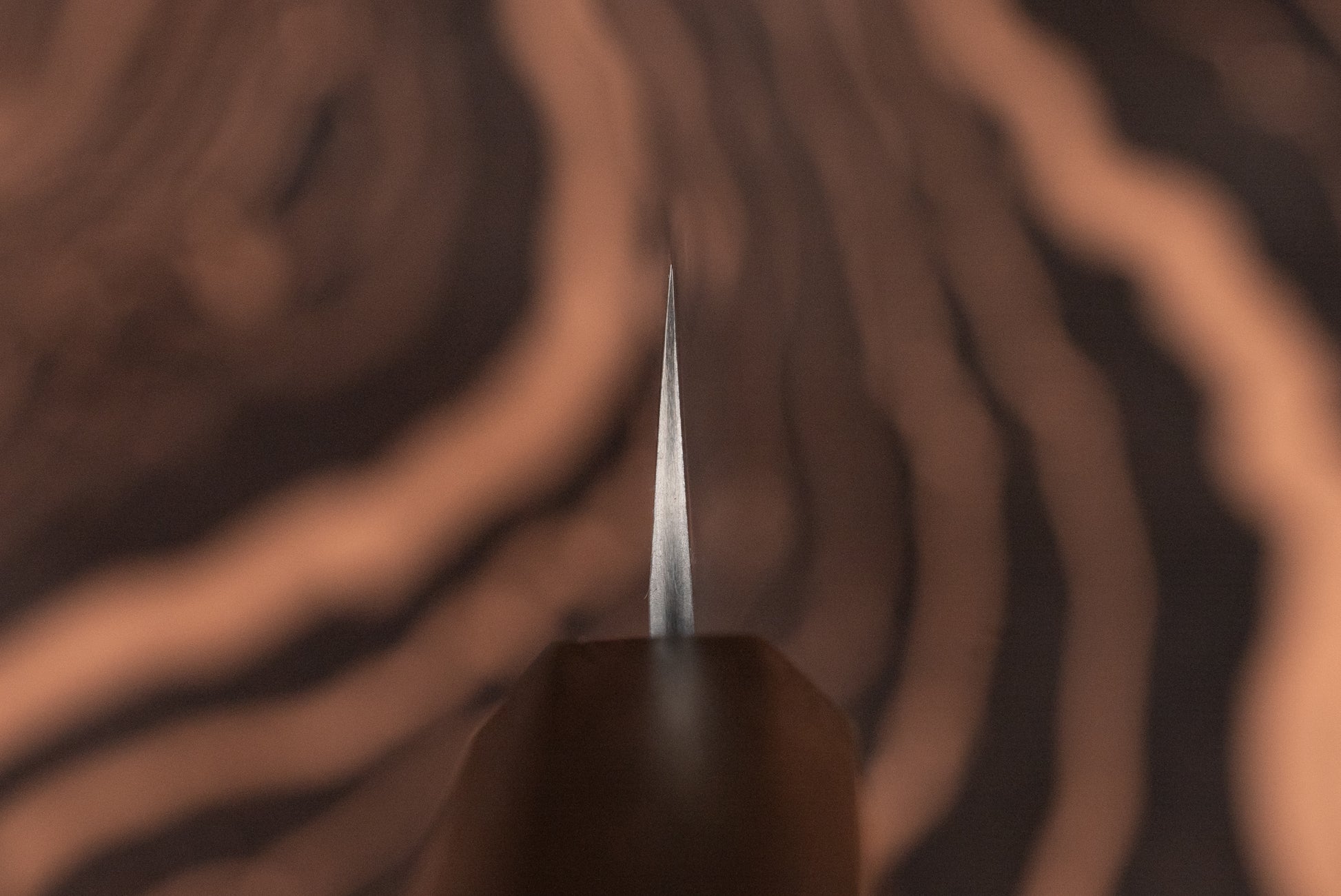 Nigara VG XEOS Tsuchime Damascus Petty 160mm knife with a wooden handle, showcasing a sharp metal blade tip against a blurred wood-grain background, ideal for precise cutting tasks.