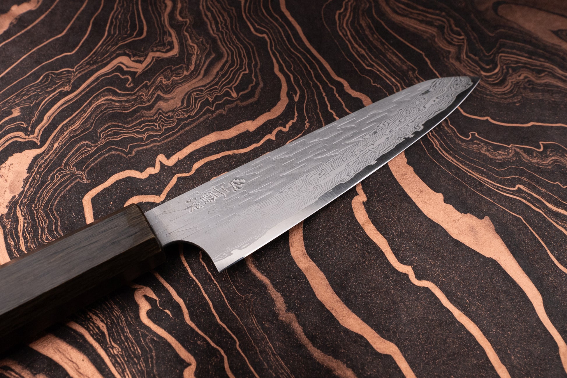Nigara VG XEOS Tsuchime Damascus Petty 160mm knife with a Damascus-style, hammered blade and dark octagonal wooden handle, displayed on a black-and-copper marbled surface, ideal for precise kitchen tasks.