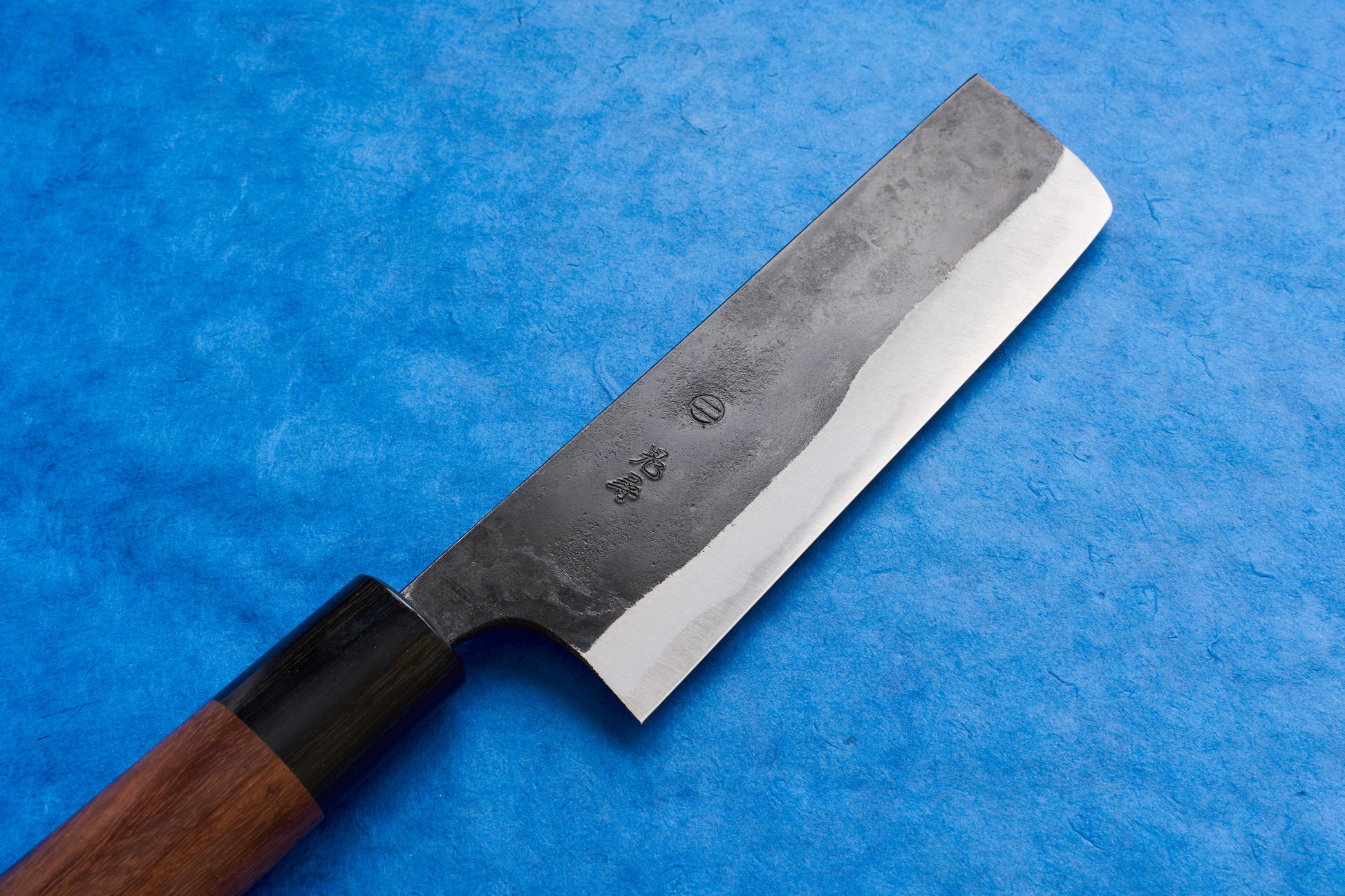Onihiro Shiroichi Kurouchi Nakiri 135mm knife, featuring a straight rectangular blade with a visible hamon, kurouchi finish, and a traditional wooden handle with a black ferrule, ideal for precise vegetable chopping.