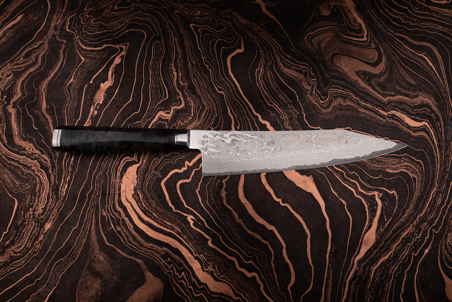 Ryusen Oukokuryu Gyuto 210mm knife with a Damascus-patterned blade and dark handle, showcased on a marbled surface echoing the knife's intricate design, embodying high-end Japanese craftsmanship.