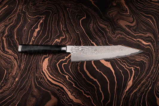 Ryusen Oukokuryu Gyuto 210mm knife with a Damascus-patterned blade and dark handle, showcased on a marbled surface echoing the knife's intricate design, embodying high-end Japanese craftsmanship.