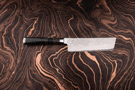 Ryusen Oukokuryu Nakiri 155mm knife features a rectangular Damascus-pattern blade and dark wood handle, elegantly displayed on a marbled surface, embodying high-end Japanese design and exceptional craftsmanship.