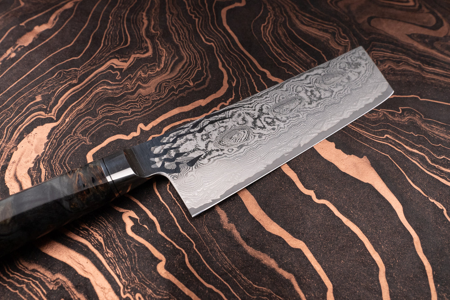 Ryusen Oukokuryu Nakiri 155mm, a Damascus-style cleaver, features a layered blade and stabilized wood handle, perfect for precise vegetable chopping, showcased against a complementary patterned surface.