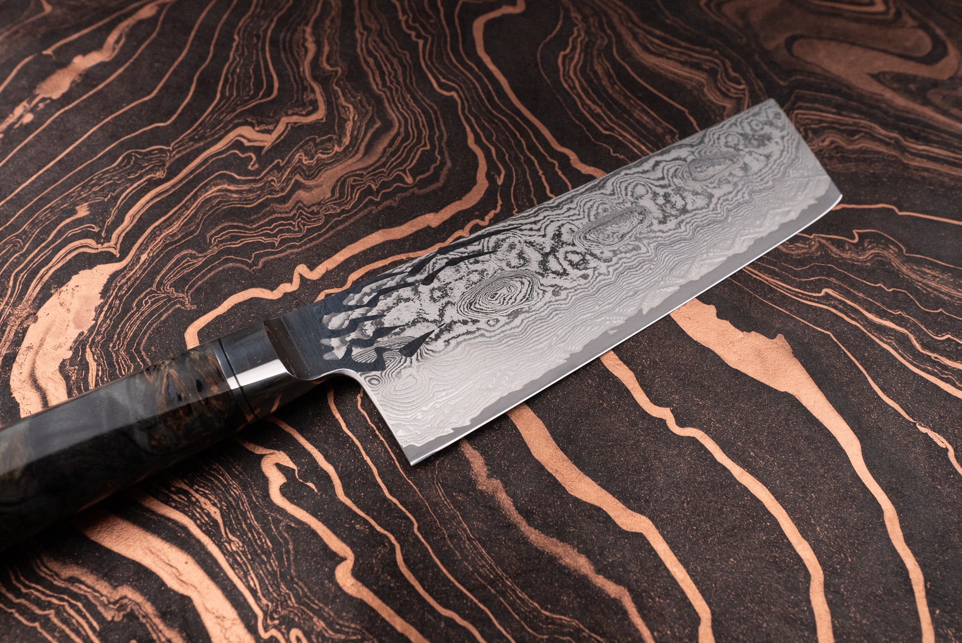 Ryusen Oukokuryu Nakiri 155mm, a Damascus-style cleaver, features a layered blade and stabilized wood handle, perfect for precise vegetable chopping, showcased against a complementary patterned surface.