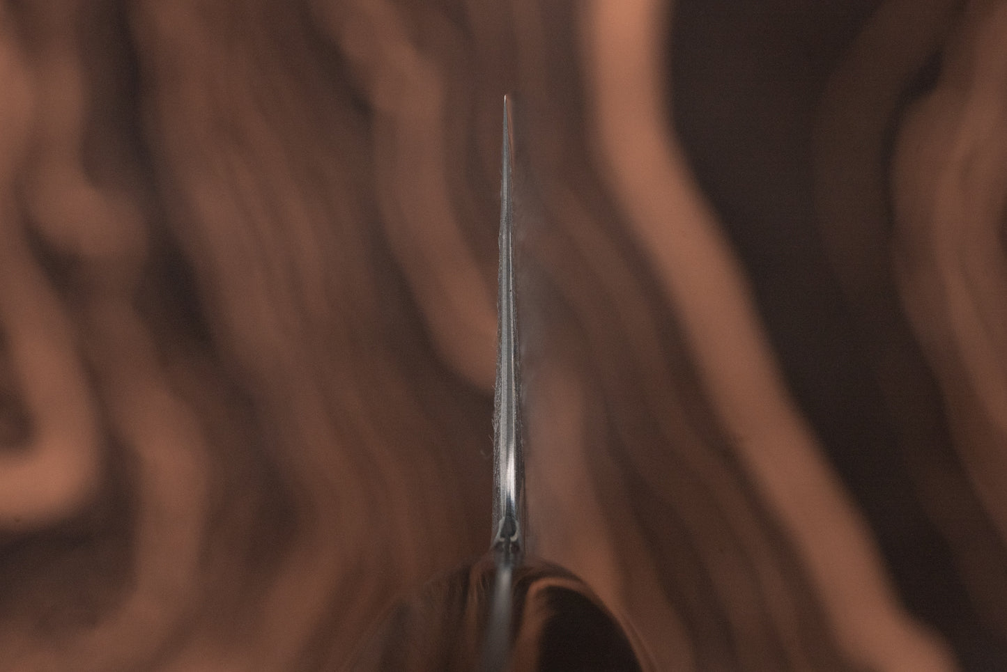 Ryusen Oukokuryu Nakiri 155mm stands vertically, showcasing its thin, sharp edge against a swirling wood-grain background, emphasizing its precision and modern Japanese craftsmanship for vegetable chopping.