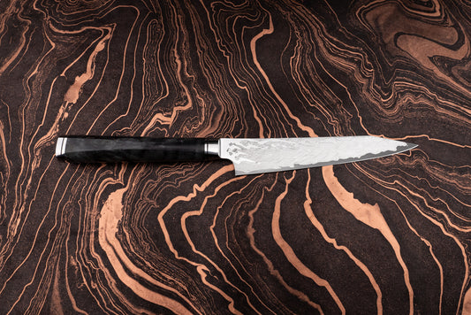 Ryusen Oukokuryu Petty 135mm knife with a Damascus-steel blade and a dark handle, showcased on a rich, patterned surface, epitomizing high-end Japanese craftsmanship and precision for smaller kitchen tasks.