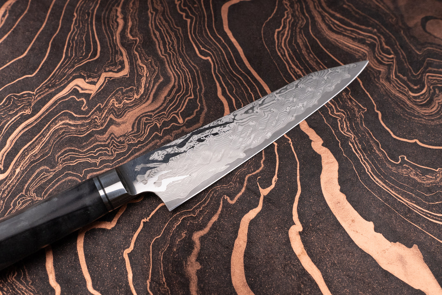 Ryusen Oukokuryu Petty 135mm displayed on a marbled surface, showcasing its Damascus-steel blade and dark handle. Perfect for precision tasks, embodying Japanese craftsmanship and modern design excellence.