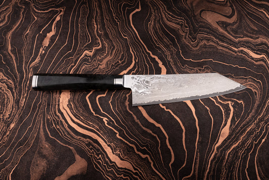 Ryusen Oukokuryu Santoku 170mm knife with a Damascus-style blade showcasing intricate layered patterns and a sleek black handle, resting on a dark, copper-streaked surface.