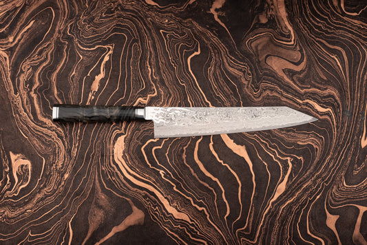 Ryusen Oukokuryu Sujihiki 260mm knife with a 98-layer Damascus-steel blade and a dark polished handle, ideal for precise slicing of meats and fish, showcased on a dark veined surface.