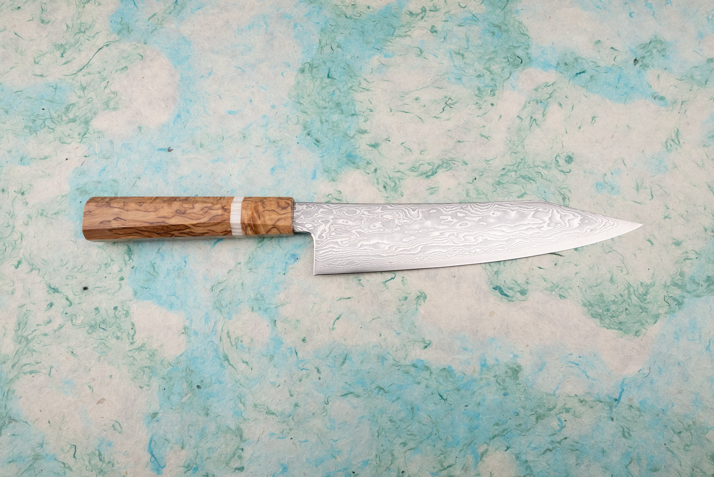Ryusen Fukakuryu KAI Gyuto 210mm knife with a Damascus-pattern blade and burl wood handle, showcased on a mottled blue-green surface, exemplifying Japanese craftsmanship and sleek design.