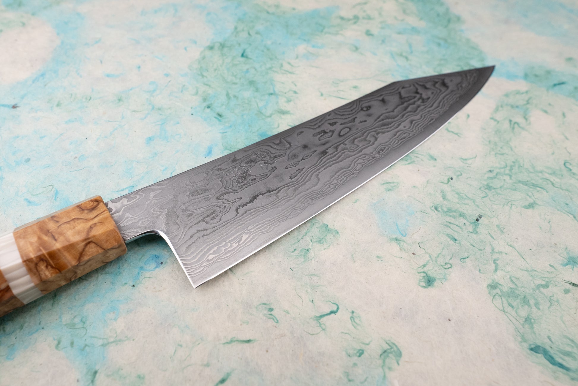 Ryusen Fukakuryu KAI Gyuto 210mm knife, showcasing a 63-layer Damascus steel blade with a wavy pattern. The handle is a hybrid wood-resin blend, resting on a marbled surface.