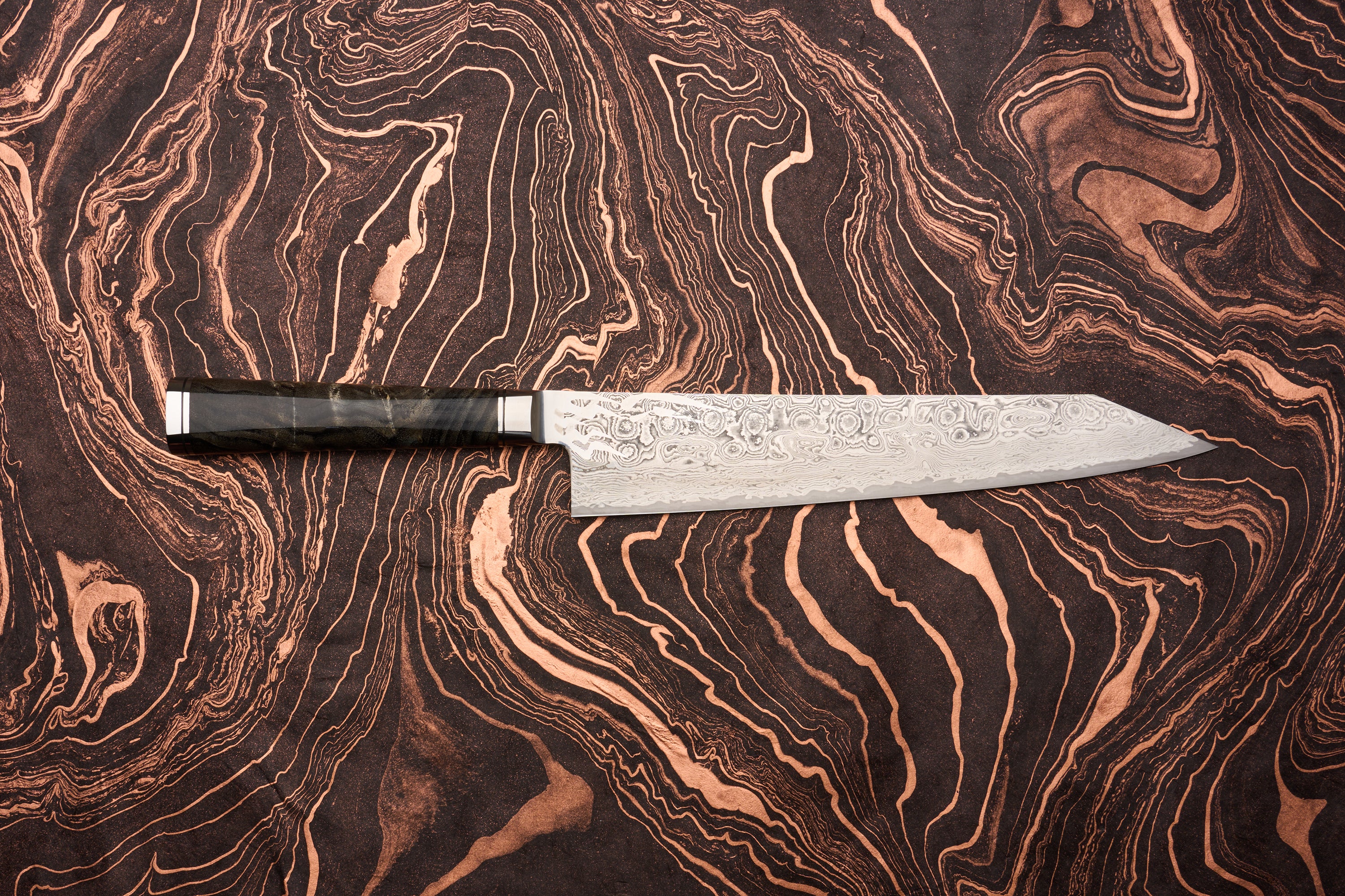 Ryusen Oukokuryu Gyuto 240mm knife features a distinctive Damascus steel blade with swirling patterns, set against a marbled black and copper background, showcasing its elegant design and craftsmanship.