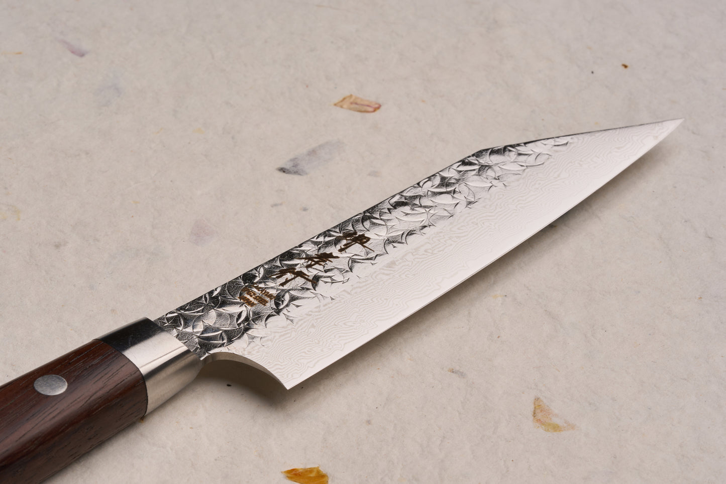 Sakai Takayuki SG2 Tsuchime Damascus Western Kengata Petty 120mm knife, features a patterned blade with subtle hammer marks and a forged steel bolster, complemented by a riveted dark wooden handle.
