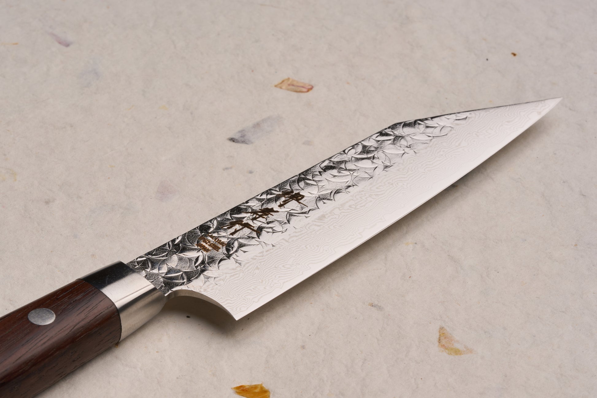 Sakai Takayuki SG2 Tsuchime Damascus Western Kengata Petty 120mm knife, features a patterned blade with subtle hammer marks and a forged steel bolster, complemented by a riveted dark wooden handle.