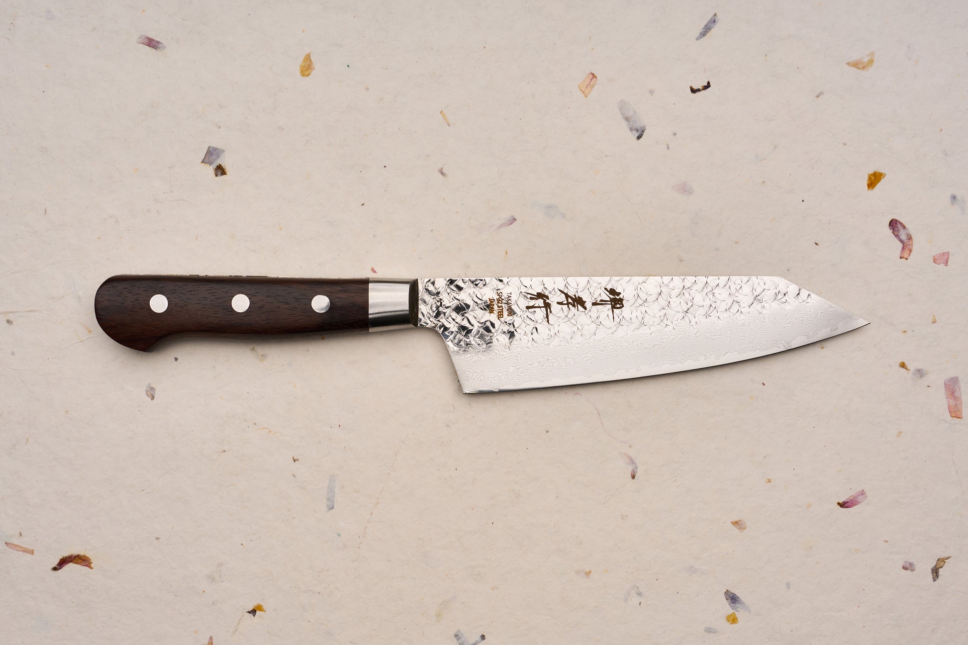 Sakai Takayuki SG2 Tsuchime Damascus Western Kengata Santoku 160mm knife with a dark wooden handle, distinctive hammered blade finish, and engraved Japanese characters, displayed on a textured handmade-paper background.