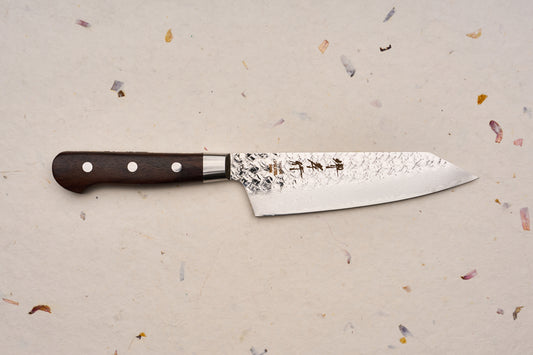 Sakai Takayuki SG2 Tsuchime Damascus Western Kengata Santoku 160mm knife with a dark wooden handle, distinctive hammered blade finish, and engraved Japanese characters, displayed on a textured handmade-paper background.