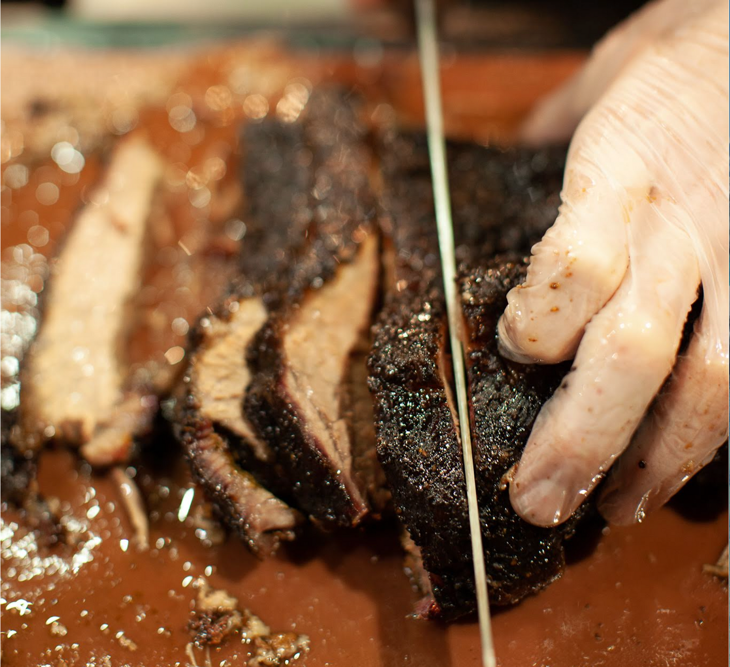 Close-up of a smoked beef brisket being sliced during the Prairie Dog Brewing X Knifewear Brisket Smoking Class in Calgary, showcasing its peppery crust, pink smoke ring, and juicy interior.