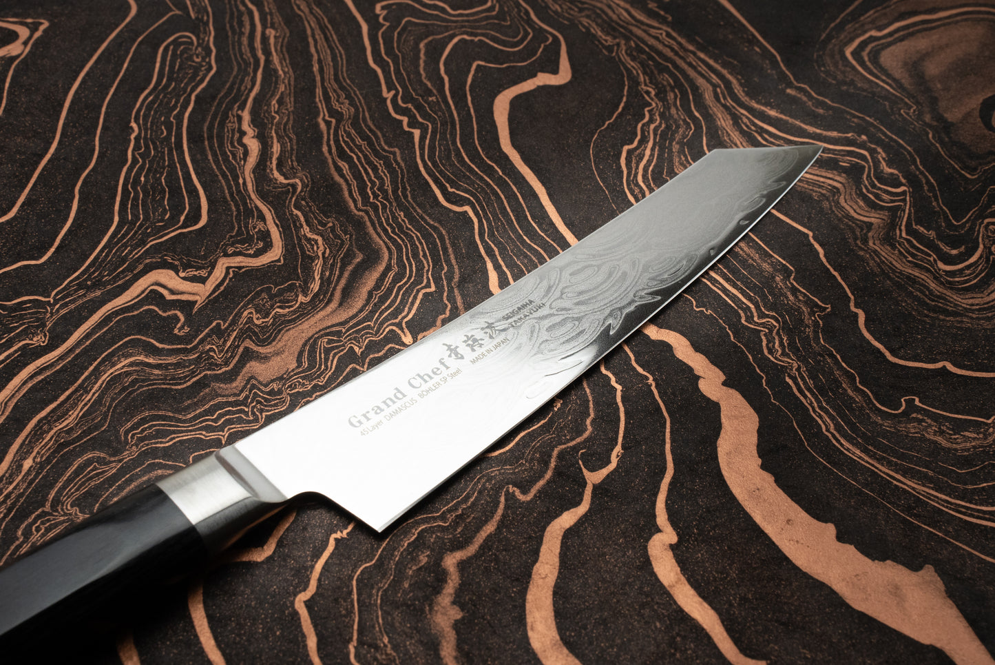 Sakai Takayuki Grand Chef Seigaiha Kengata Petty 150mm knife with a Damascus-patterned blade and dark handle, displayed on a marbled surface, highlighting its craftsmanship and Japanese origin.