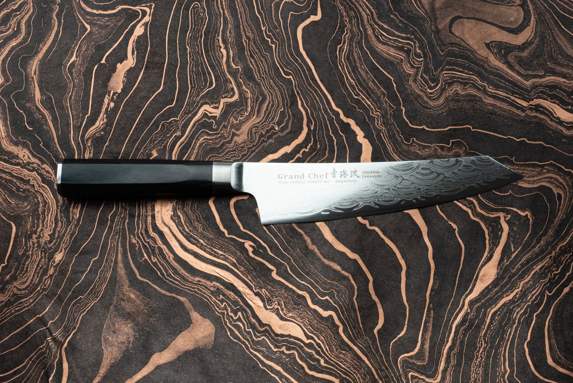 Sakai Takayuki Grand Chef Seigaiha Kengata Gyuto 190mm knife with a Damascus-steel pattern blade and octagonal black handle, elegantly displayed on a marbled surface, showcasing Japanese craftsmanship.