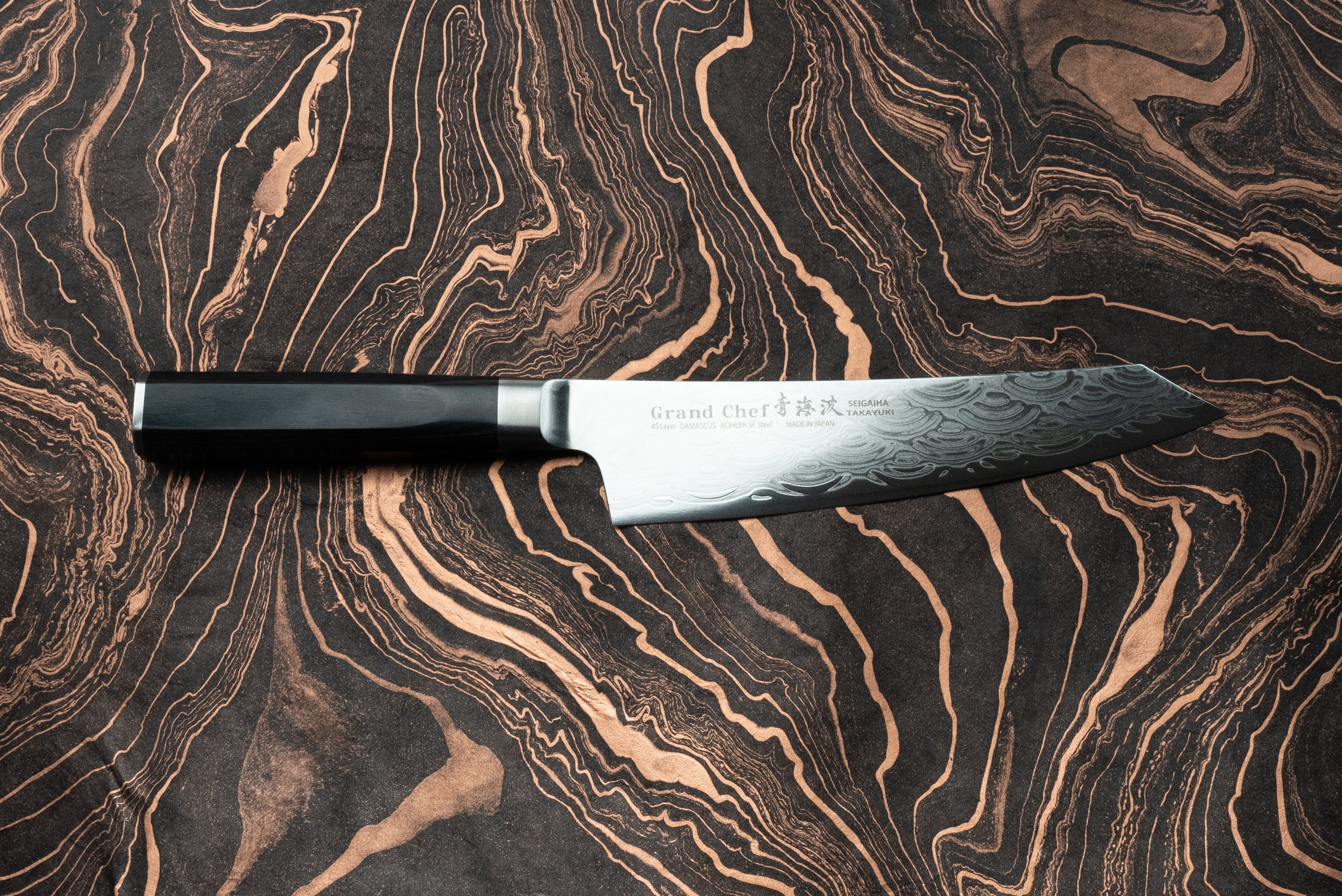 Sakai Takayuki Grand Chef Seigaiha Kengata Gyuto 190mm knife with a Damascus-steel pattern blade and octagonal black handle, elegantly displayed on a marbled surface, showcasing Japanese craftsmanship.