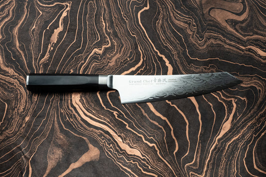 Sakai Takayuki Grand Chef Seigaiha Kengata Gyuto 190mm knife with a Damascus-steel pattern blade and octagonal black handle, elegantly displayed on a marbled surface, showcasing Japanese craftsmanship.