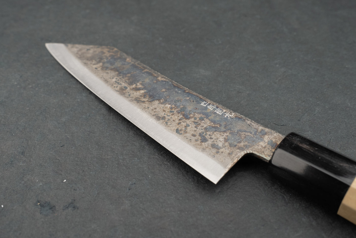 Shiro Kunimitsu Aogami Kurouchi Chikuzen Bunka 160mm knife with a carbon-steel patina blade, stamped Japanese characters, and an octagonal wooden handle, exemplifying traditional Japanese craftsmanship for precise kitchen cutting.