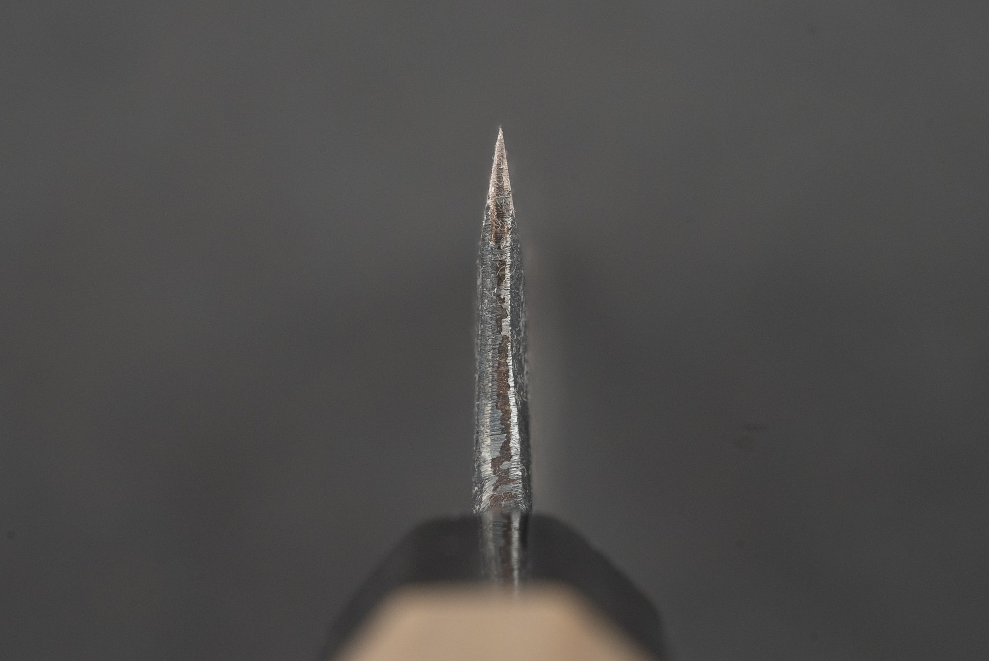 Macro view of the Shiro Kunimitsu Aogami Kurouchi Chikuzen Ko-Bunka 140mm knife tip, showcasing its robust bevel and slightly visible handle, epitomizing Japanese craftsmanship in kitchen knives.