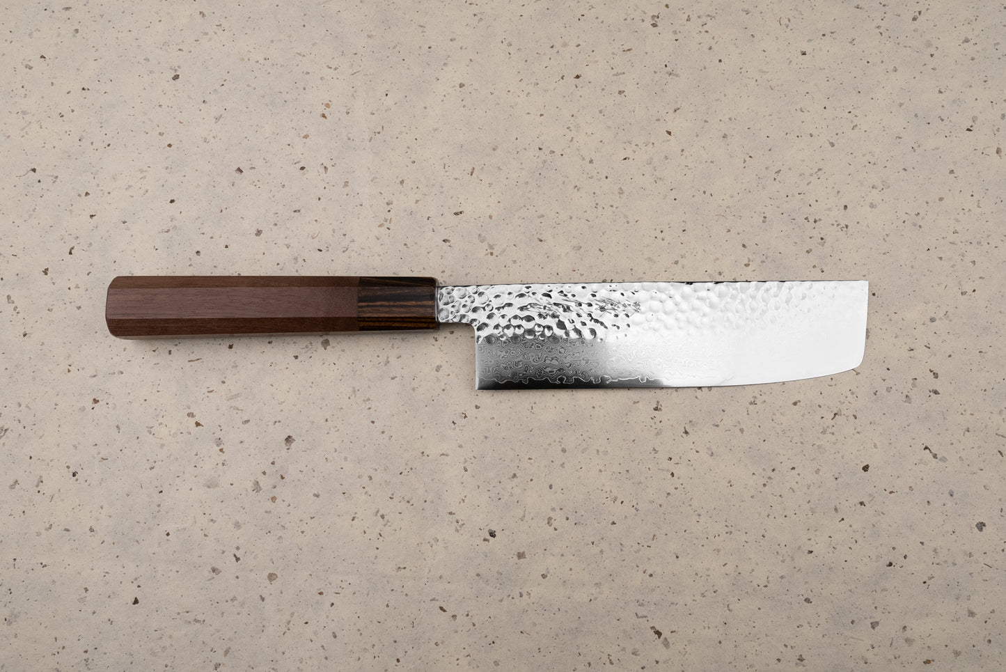 The Touroku Sakai Yukage Nakiri 160mm rests on a speckled counter, showcasing its straight rectangular blade with hammered and Damascus patterns, paired with a traditional dark wooden octagonal handle.