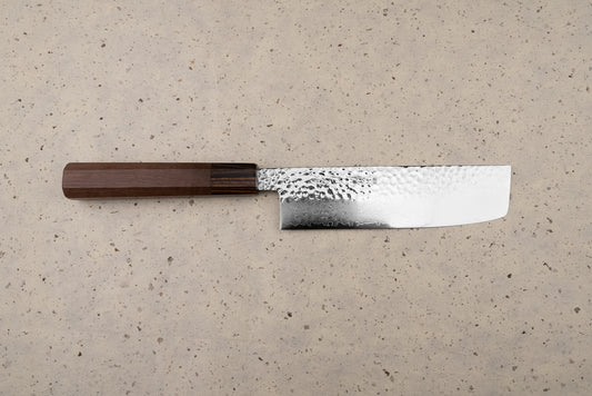 The Touroku Sakai Yukage Nakiri 160mm rests on a speckled counter, showcasing its straight rectangular blade with hammered and Damascus patterns, paired with a traditional dark wooden octagonal handle.
