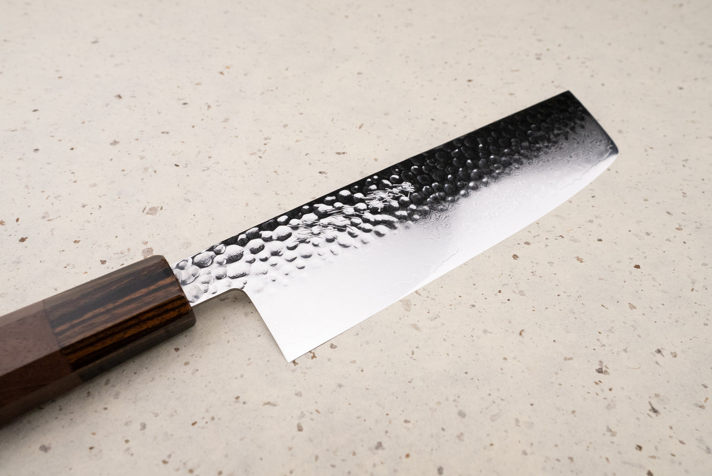Touroku Sakai Yukage Nakiri 160mm displayed on a stone countertop, featuring a hammered tsuchime pattern and Damascus-style waves on the blade, with an octagonal dark wood handle.