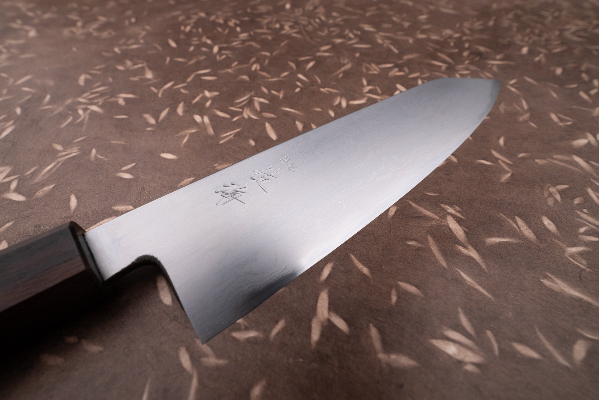 Touroku Sakai Aogami Damascus Kiritsuke Gyuto 210mm, featuring an engraved polished steel blade and dark wooden handle, showcased on a decorative surface, embodying Japanese craftsmanship excellence.
