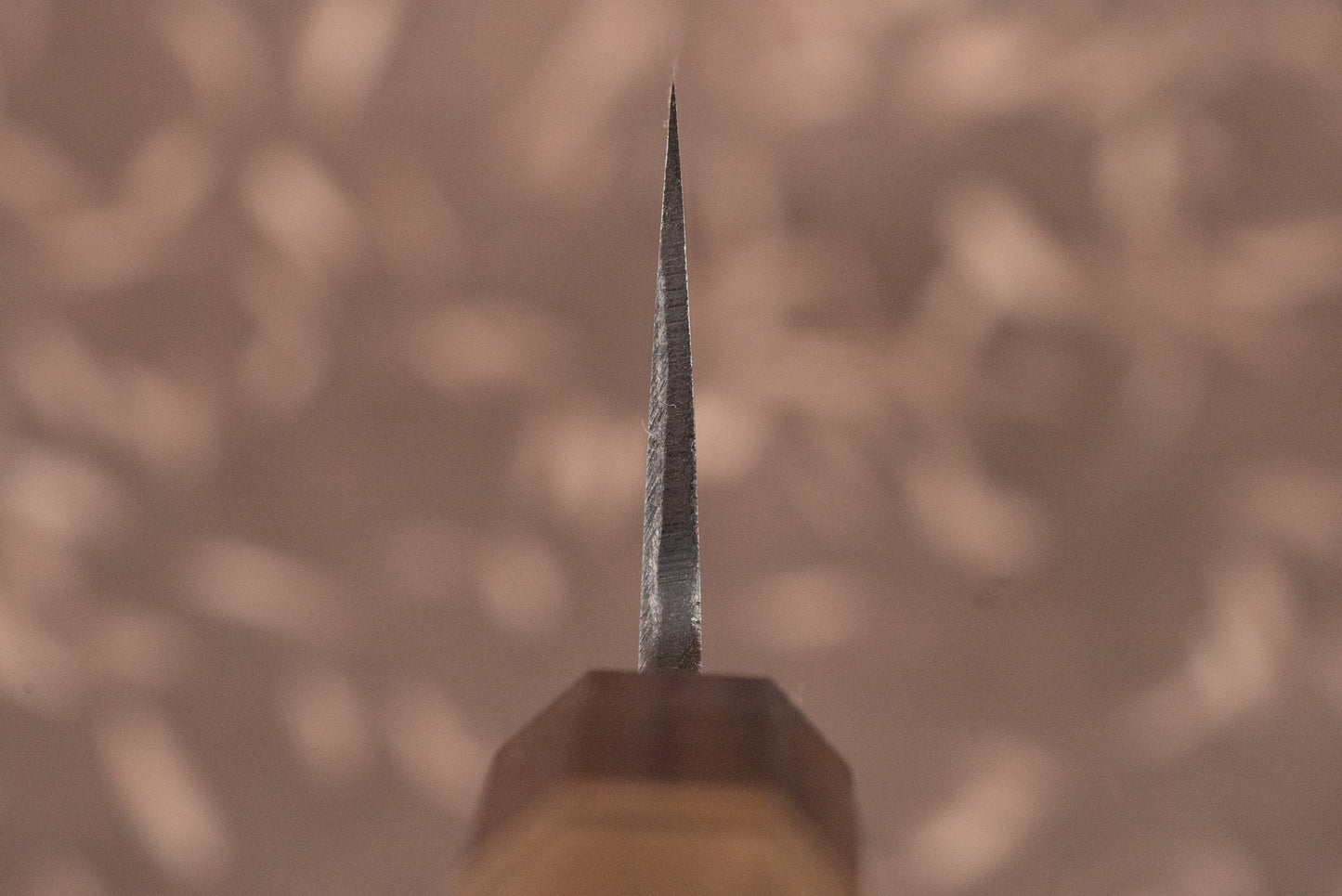 Close-up of the Touroku Sakai Aogami Damascus Kiritsuke Gyuto 210mm's tip, highlighting its precise bevelled edge and wood-handled ferrule, epitomizing expert Japanese craftsmanship and multi-purpose utility in the kitchen.