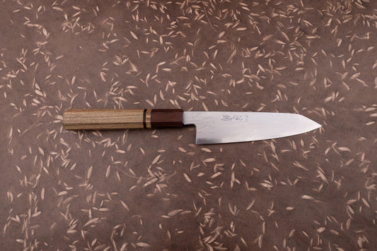 Touroku Sakai Aogami Damascus Kiritsuke Petty 150mm knife with a laminated steel blade and octagonal wooden handle on a brown surface with leaf motifs, ideal for precise kitchen tasks.