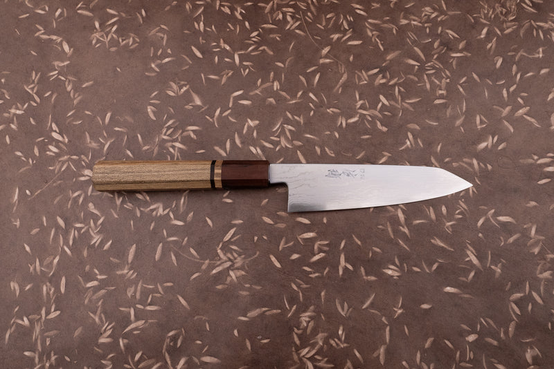 Touroku Sakai Aogami Damascus Kiritsuke Petty 150mm knife with a laminated steel blade and octagonal wooden handle on a brown surface with leaf motifs, ideal for precise kitchen tasks.